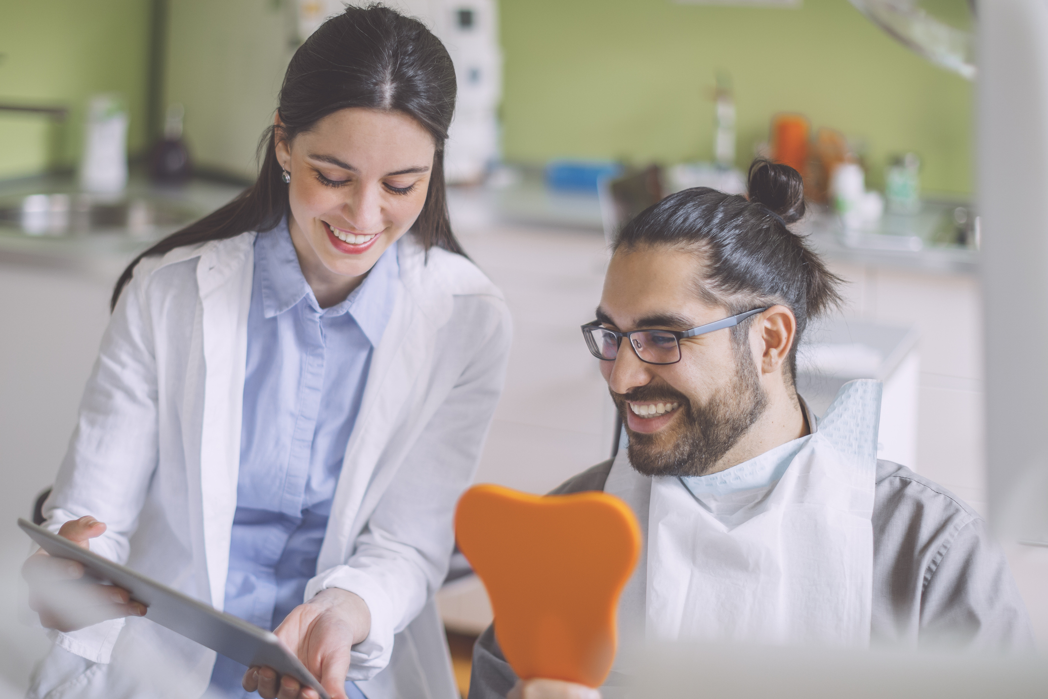 Dentist showing a dental model to a smiling patient in a clinic.